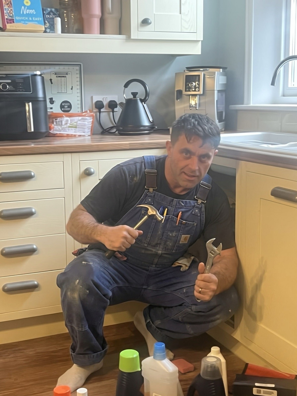 WHINN handyman working beside a kitchen sink, holding a hammer and adjustable spanner